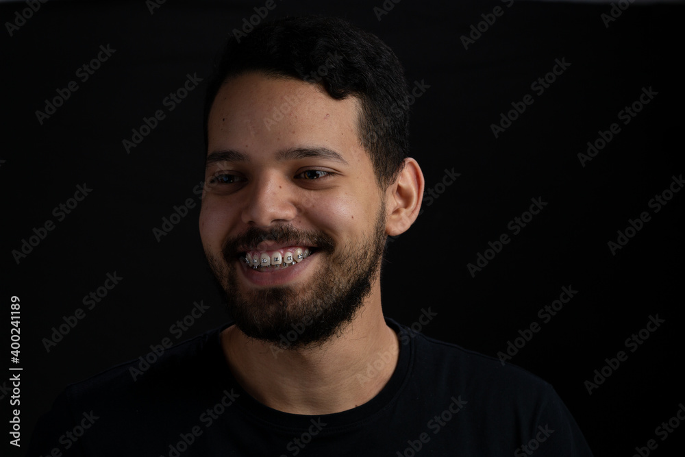 Young bearded man headshot over black background. He looks happy with a big smile.