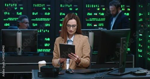 Young beautiful caucasian female system administrator sitting at workplace holding tablet and solving work questions. Work in server room. photo