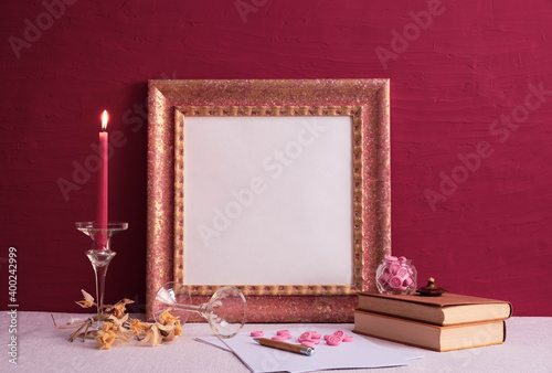 old books, a candlestick on a long leg with a burning candle, an old photo frame on red and a decor background