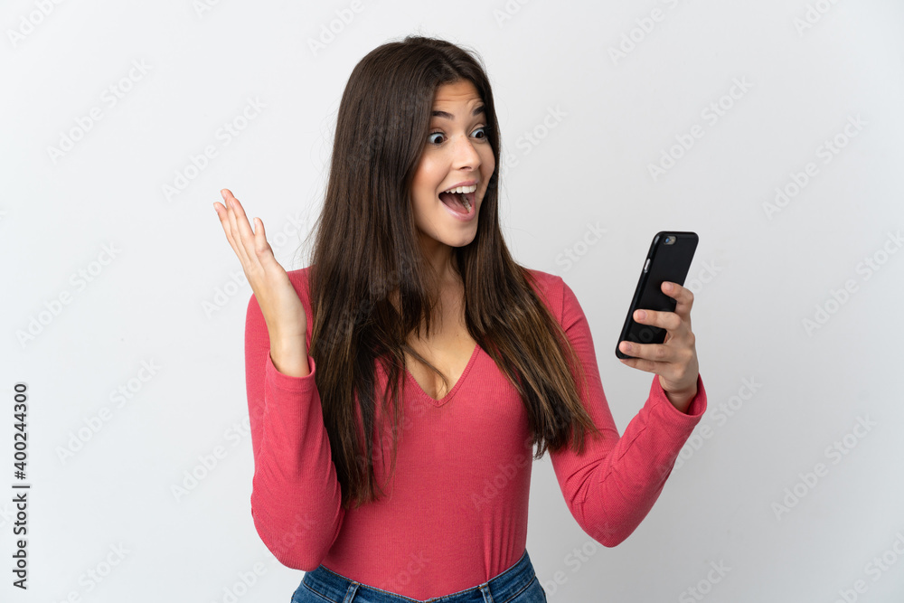 Teenager Brazilian girl isolated on white background looking at the camera while using the mobile with surprised expression Teenager Brazilian girl isolated on white background looking at the camera while using the mobile with surprised expression