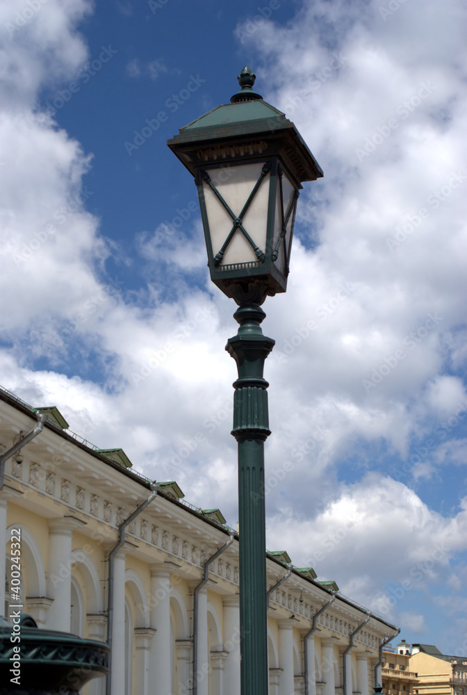 Black and white lamp post with electrical street lantern in retro style in front of cityscape in the bright sunny day vertical view closeup