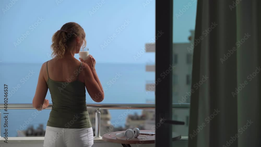 A woman on the balcony drinks milk and admires the sea and the sunset. A woman on the balcony drinks milk and admires the sea and the sunset.