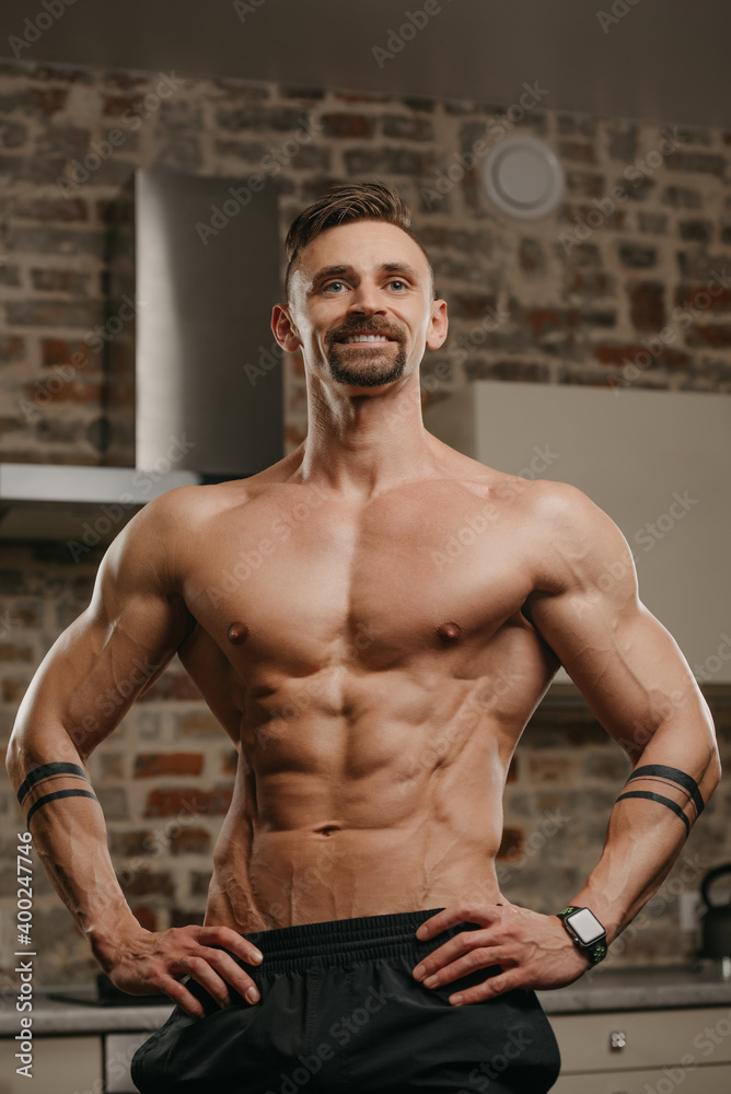 A muscular man with a beard is posing in his apartment. An athletic guy with tattoos on his forearms is demonstrating his sporty physique at home. An athlete is relaxing after hard training. A muscular man with a beard is posing in his apartment. An athletic guy with tattoos on his forearms is demonstrating his sporty physique at home. An athlete is relaxing after hard training.