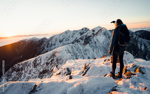 Woman stands with backpack on big rock on background of mountrains in winner.Hiking Travel Lifestyle adventure concept active vacations outdoor snow mountain on background photo