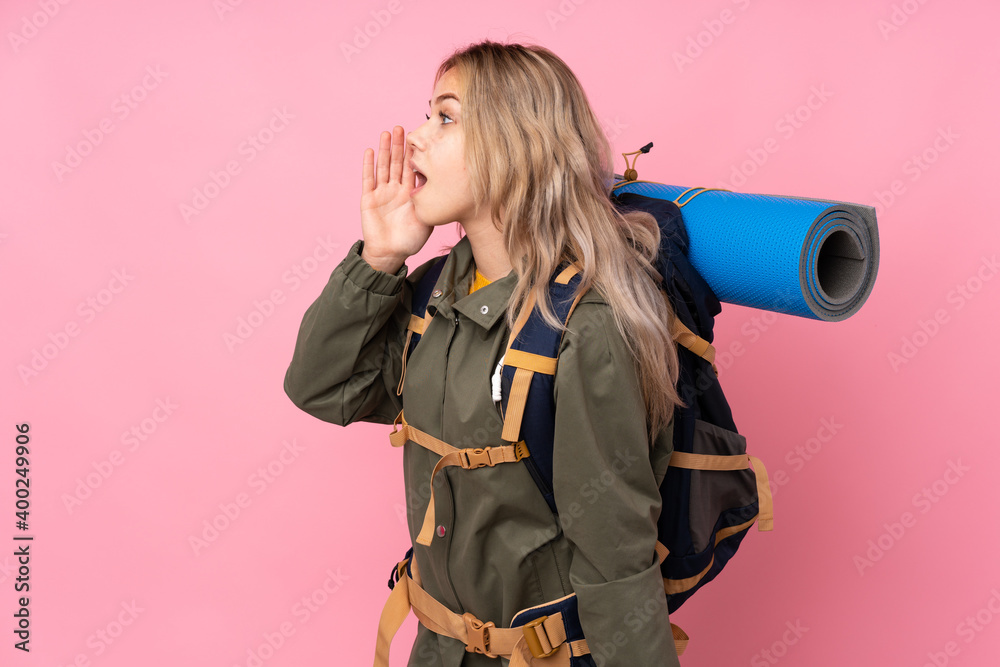 Teenager Russian mountaineer girl with a big backpack isolated on pink background shouting with mouth wide open to the lateral Teenager Russian mountaineer girl with a big backpack isolated on pink background shouting with mouth wide open to the lateral