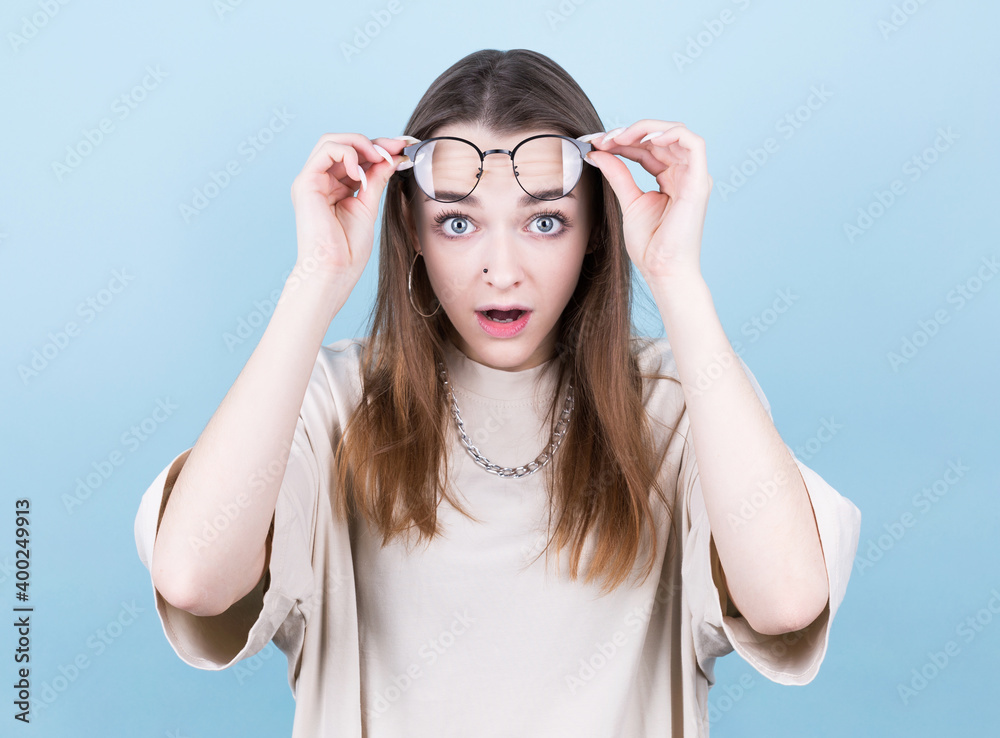 Portrait of a surprised young beautiful girl in eyeglasses looking at camera while raised up glasses. Isolated over gray background Portrait of a surprised young beautiful girl in eyeglasses looking at camera while raised up glasses. Isolated over gray background