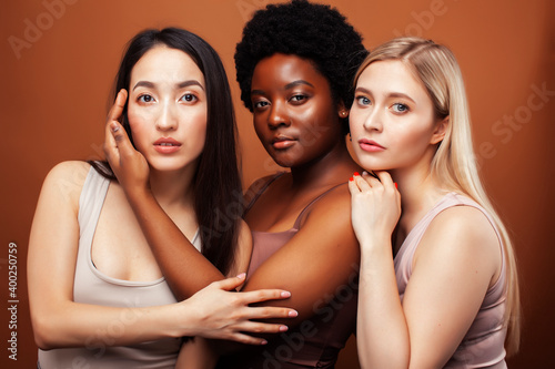 young pretty asian, caucasian, afro woman posing cheerful together on brown background, lifestyle diverse nationality people concept