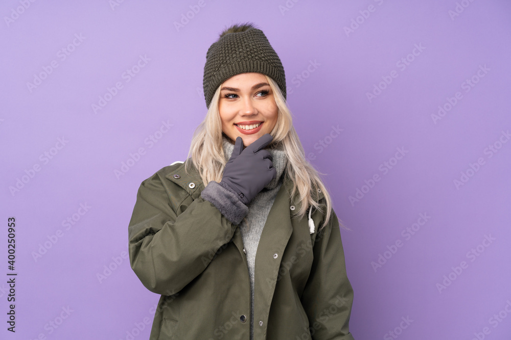 Teenager blonde girl with winter hat over isolated purple background looking to the side Teenager blonde girl with winter hat over isolated purple background looking to the side