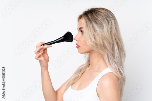 Teenager blonde girl over isolated white background holding makeup brush