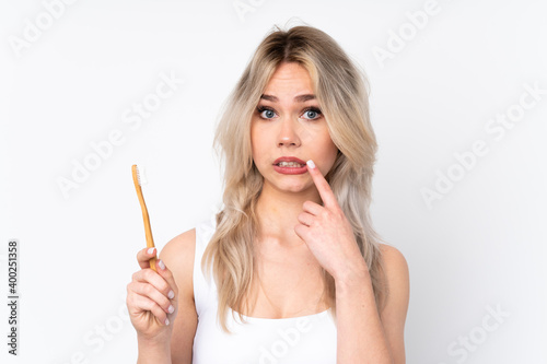 Teenager blonde girl over isolated white background with a toothbrush and happy expression