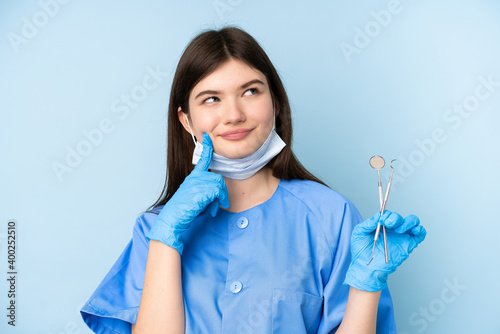 Young dentist woman holding tools over isolated blue background thinking an idea