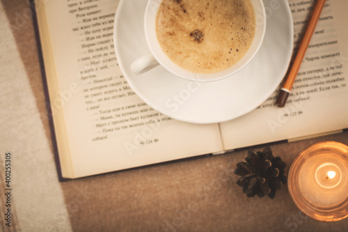 A cup of hot latte and a book by candlelight, warm and cream toned cozy image, winter atmosphere and mood
