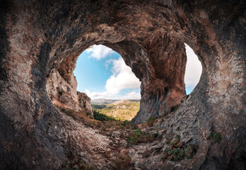 Fotobehang Cappuccinokleur Panoramic of a large cave with two entrances. Interior of a cavern with a stone arch at the entrance. Cueva de los Arcos, Spain. Ancient ancestral cave in the mountain shows us a beautiful landscape  © Hector
