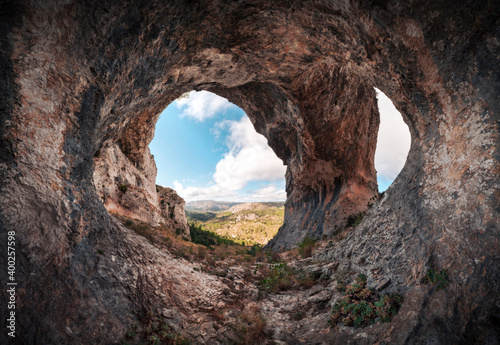 Panoramic of a large cave with two entrances. Interior of a cavern with a stone arch at the entrance. Cueva de los Arcos, Spain. Ancient ancestral cave in the mountain shows us a beautiful landscape