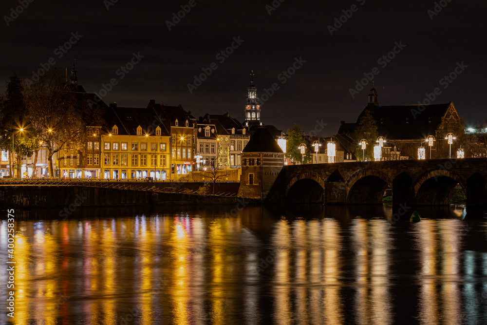 Maastricht, Netherlands 12-11-2020 illuminated skyline with christmas decorations of downtown Maastricht and the old bridge with arches and reflections in the river Meuse
