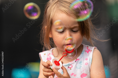 Little girl blowing soap bubbles outdoors at summer