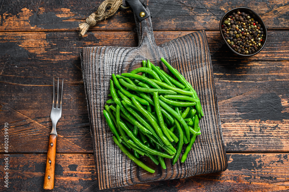 Fresh green beans on a cutting board. Dark wooden background. top view