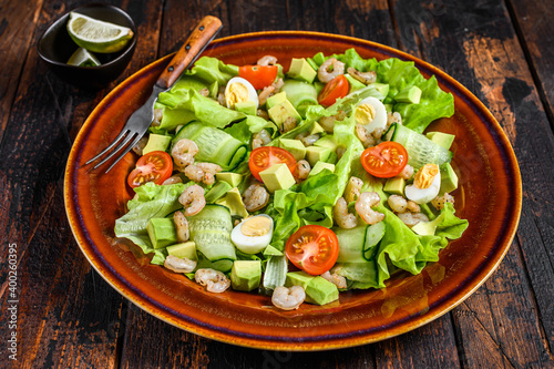 Fresh avocado, shrimps, prawns salad with lettuce green mix, cherry tomatoes and olive oil. Dark wooden background. top view