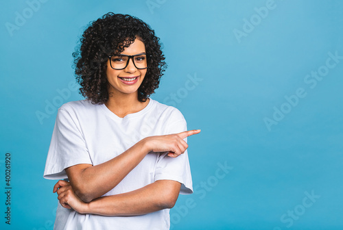 Portrait of a happy young african american woman pointing fingers away at copy space isolated over blue background.