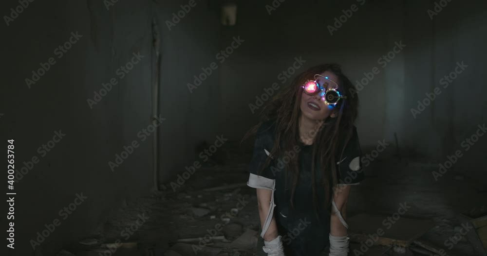 Young woman wearing trendy goggles with a shining light and illuminated frames standing grinning seductively at the camera in the darkness of an abandoned building Young woman wearing trendy goggles with a shining light and illuminated frames standing grinning seductively at the camera in the darkness of an abandoned building
