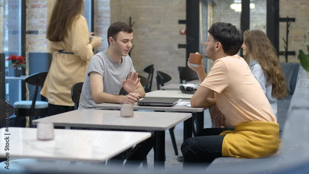 Side view of positive young men talking at the table in cafe as woman meeting friend at the background. Relaxed carefree Caucasian people resting with coffee indoors. Cinema 4k ProRes HQ. Side view of positive young men talking at the table in cafe as woman meeting friend at the background. Relaxed carefree Caucasian people resting with coffee indoors. Cinema 4k ProRes HQ.