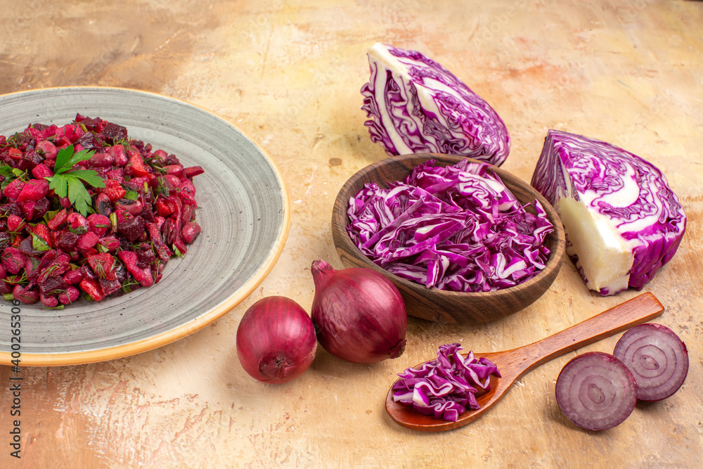 top view beetroot salad on a ceramic plate with red onions and a bowl of chopped red cabbage on a wooden background