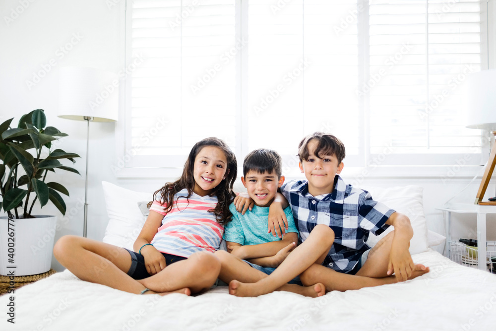 Portrait of smiling brothers ( 6-7, 8-9 ) and sister ( 10-11 ) sitting on bed Portrait of smiling brothers ( 6-7, 8-9 ) and sister ( 10-11 ) sitting on bed