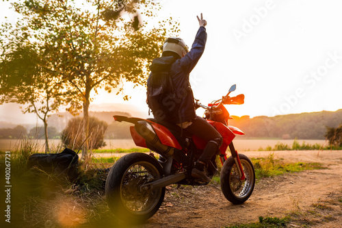 Enduro racer sitting on his motorcycle watching the sunset doing victory sign with hand
travel motorcycle off road Motorcyclist
