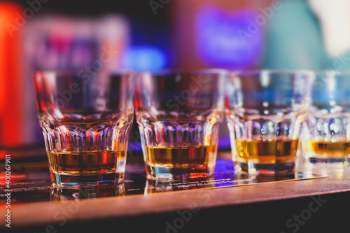 Beautiful row of different colored alcohol cocktails on a party, whiskey, scotch whisky, and others, glasses on a bar counter, bar stand, with bartender in the background