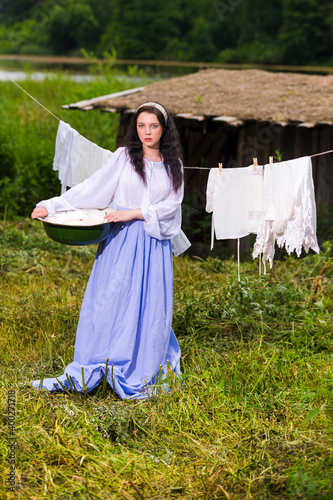 Portrait of Caucasian Brunette Girl in Traditional Rural Dress Holding Basin With Linens in Countryside. © danmorgan12