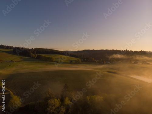 Aerial view of fog creeps over forest lake on rising sun background. Landscape with autumn dawn. Wallpaper design. Dramatic view.