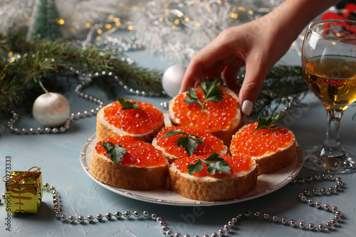 Sandwiches with red caviar on a plate against a light blue background. Festive snack. The woman reaches out to take the sandwich off the plate.