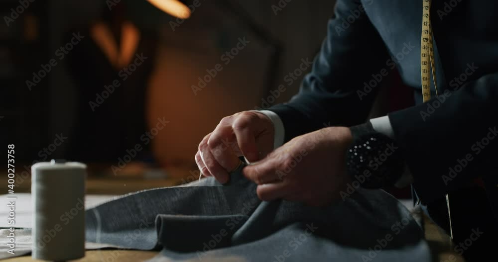 Cinematic shot of experienced tailor is sewing custom handmade high quality apparel in ancient luxury traditional tailoring atelier. Concept of industry, handmade, hand craft, couturier and tradition.