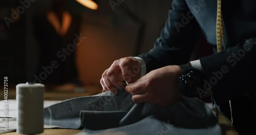 Cinematic shot of experienced tailor is sewing custom handmade high quality apparel in ancient luxury traditional tailoring atelier. Concept of industry, handmade, hand craft, couturier and tradition.