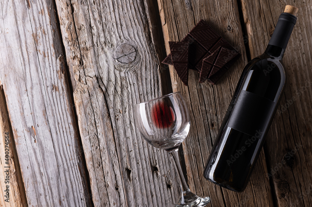 Fantastic composition with dark chocolate, elegant bottle and glass with remains of red wine on rustic wooden background. Advertising and promotion concept. Mock up. Flat lay. View from above. Fantastic composition with dark chocolate, elegant bottle and glass with remains of red wine on rustic wooden background. Advertising and promotion concept. Mock up. Flat lay. View from above.
