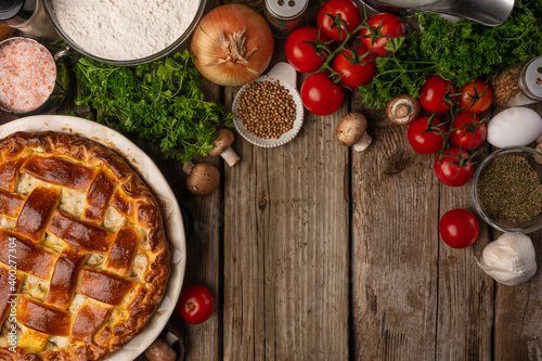 Ruddy pie with meat and mushrooms on wooden table with variety of ingredients background. Cooking process. Backstage of preparing tasty meal. View from above. Flat lay. Cookbook. Space for text.