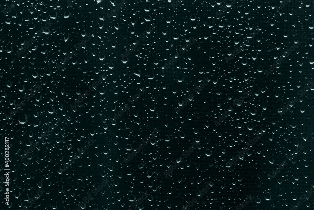 Raindrops on dark blue-green window glass as background