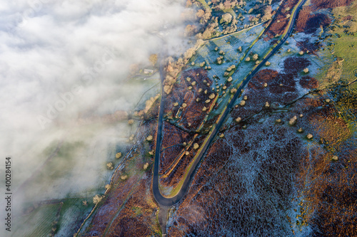 Aerial view of a narrow, winding mountain road emerging through a bank of fog and low cloud on a cold, frosty day photo