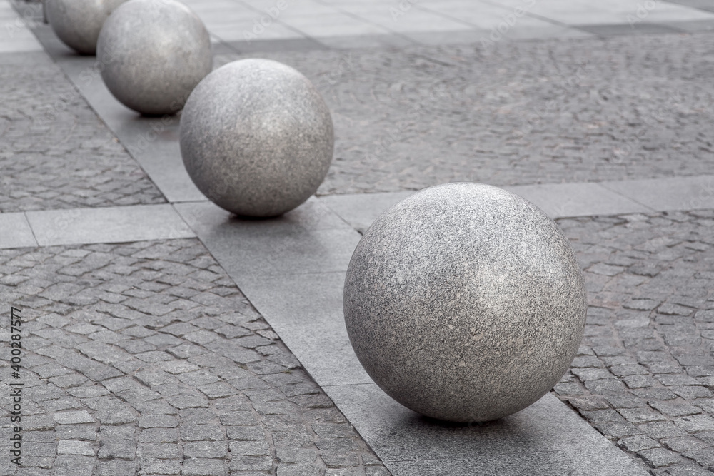 Naklejka row of granite balls on the pedestrian sidewalk paved with stone tiles, cityscape urban street architecture, nobody.