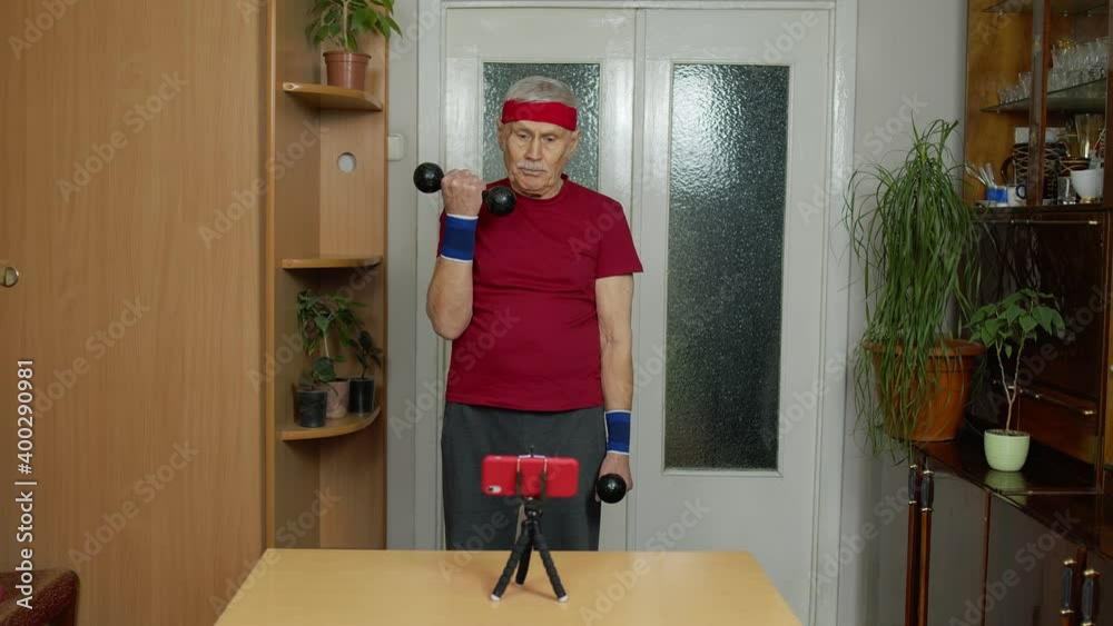 Mature man fitness trainer coach recording video online workout course with a smartphone live streaming sport exercises at home. Senior grandfather live stream, blog, vlog during coronavirus lockdown Mature man fitness trainer coach recording video online workout course with a smartphone live streaming sport exercises at home. Senior grandfather live stream, blog, vlog during coronavirus lockdown