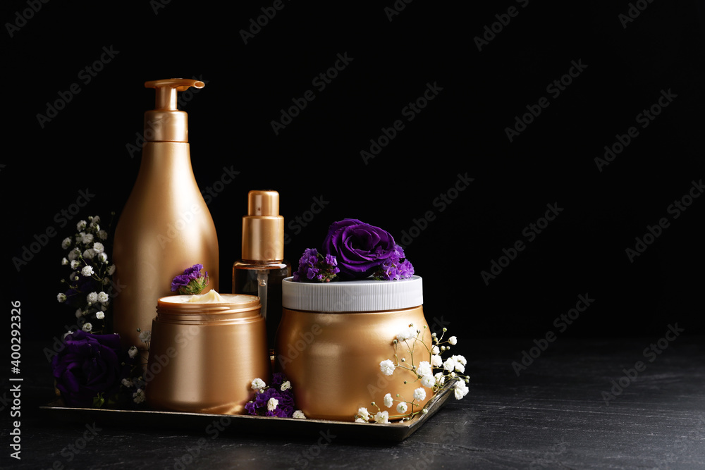 Set of hair cosmetic products and flowers on stone table against black background. Space for text Set of hair cosmetic products and flowers on stone table against black background. Space for text