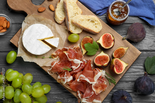 Board with delicious figs, proscuitto, cheese and grapes on grey wooden table, flat lay