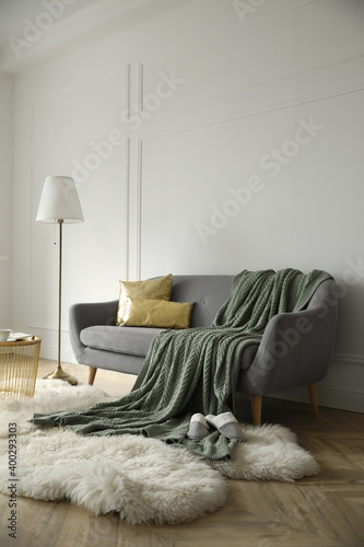 Stylish room interior with comfortable sofa, knitted blanket and lamp near white wall
