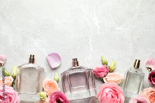 Flat lay composition of different perfume bottles and flowers on light grey marble background, space for text