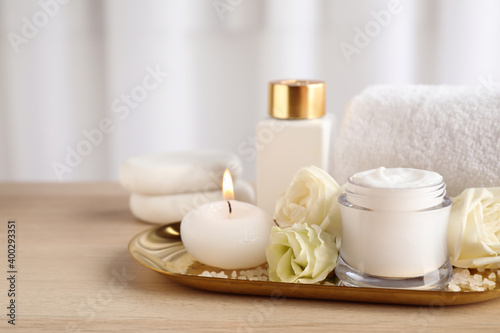 Spa composition with skin care products, flowers and candle on wooden table. Space for text