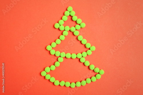 Christmas tree shape made with green fluffy balls on orange background, flat lay