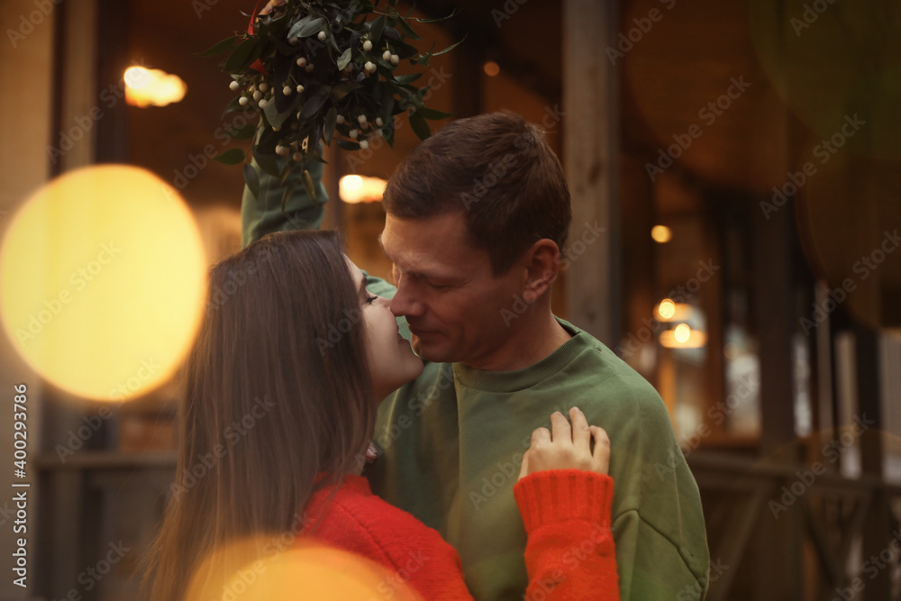 Happy couple kissing under mistletoe bunch outdoors, bokeh effect