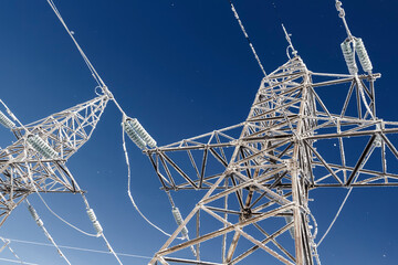 High-voltage wires and poles are covered with frost on a frosty winter day.