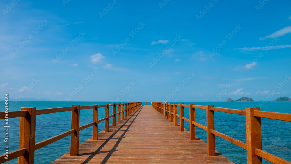 Fototapeta premium Outdoor, landscape shot of wooden walk way into the middle of the ocean. With clear blue sky and cloud with seascape island view. Tropical travel destination ideal for background with copy space.