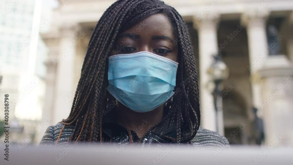 Young female executive using her laptop in the city and wearing face mask Young female executive using her laptop in the city and wearing face mask